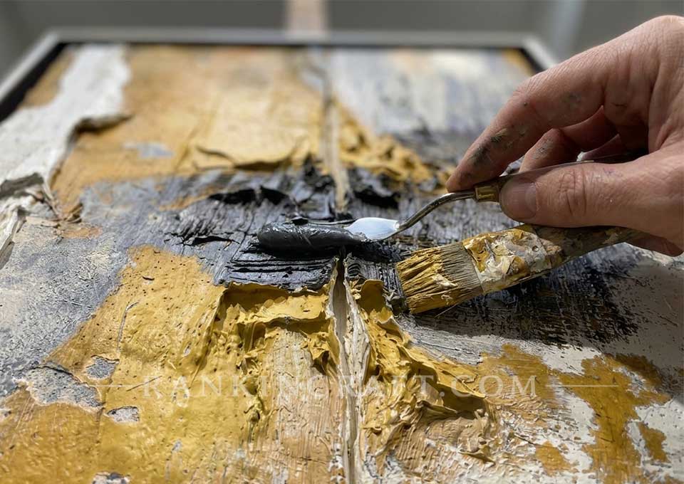 Close-up view of an artist using a palette knife to apply thick oil paint on an impasto canvas